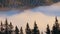 Time lapse of distant dark mountain hills covered with dense pine forest surrounded with white fast moving foggy clouds at sunrise