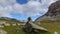 Time lapse motion. Stone pyramid on a hiking trail in the mountains, flying fluffy puffy white clouds in the bright blue sky