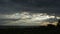 Time lapse sunset cloudscape of shore with plants shaking in wind and sunbeams breaking through grey stormy clouds