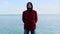 Time-lapse Unshaven young man in red jacket stands against the backdrop of the sea horizon line