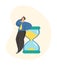 Time management concept. Businessman stands near hourglass