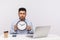 Time management. Serious displeased man employee sitting in office workplace with laptop, holding big clock