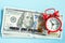 Time is money text and red alarm clock on background of American hundreds dollar bills, closeup. Creative concept quote of the day