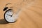 Time is running out. Black alarm clock vanishing on sand in desert