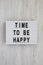 `Time to be happy` words on a lightbox on a white wooden background, top view. Overhead, from above. Flat lay. Close-up