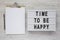 `Time to be happy` words on a modern board, clipboard with blank sheet of paper on a white wooden surface, top view. Overhead,