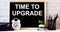 TIME TO UPGRADE is written on the chalkboard next to the white alarm clock, glasses, potted plant, and pencils in a stand