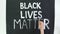 Timelapse. close-up, hand writes slogan - Black Lives Matter - with brush, using white paint on black banner, poster