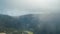 A timelapse cloud floats over the tops of the trees standing on the mountain. There is a mountain gorge below