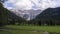 Timelapse of clouds above mountains and meadows with trees in front