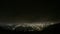 Timelapse of heavy mountain clouds, lights of night city lying below near sea