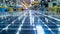 A timelapse image of a solar panel being assembled on a factory floor with workers and robotic arms seen in the