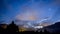 Timelapse night sky stars and moon across fast clouds with mountain background