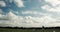 Timelapse with sheep and a woolly sky. Cloudy weather over a herd of black and white sheep and lambs grazing on a rough meadow.