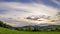 Timelapse of sunset over a mountain lying above a village of dense colorful clouds moving over a natural landscape full of trees a