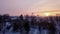 Timelapse, winter sunset over the snow-covered city, dark outlines of bare trees, the roofs of houses, the orange sun