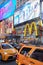 Times Square show billboards with people, yellow taxi traffic at night in New York