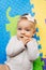 Tiny baby girl with a flower on her head in a white blouse lies on a multi-colored rug with her hands in her mouth