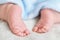 Tiny bare legs and feet of newborn covered with a blue soft warm blanket. Little baby sleeps on white blanket on bed. Dermatology