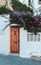 Tiny brown door on a white wall outside in Spain. Entrance to the local house or apartment for rent. Covered with beautiful violet