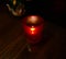 A tiny flame flickers in a red translucent votive candle holder, illuminating a glossy wooden table top