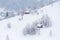 Tiny houses stand atop a snowy hill, surrounded by a fierce snowstorm.