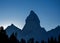 Tiny mountain climber with outstretched arms at the summit of a hill. Sky background with space for copy.