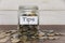 Tips label on coin jar on top of wooden desk with asorted coins background.