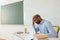 Tired african american teacher sitting at table with laptop and coffee cup