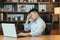 Tired Asian works late, in a classic office, working on a laptop, pensive holding his hand behind his head