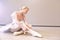 Tired ballerina sitting in a dance studio and puts on pointe shoes over beige wall background isolated