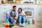 Tired black couple sitting on floor among cleaning supplies after finishing cleanup, looking at each other and smiling
