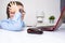 A tired boy, schoolboy in blue shirt sitting by the table with a laptop on it at home, difficulties of e-learning and online