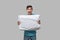 Tired brunet man in a blue tee holding white pillow isolated over grey background.