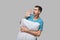 Tired brunet man in a blue tee shout holding white pillow isolated over grey background.