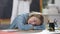 Tired Caucasian schoolgirl sleeping on desk in classroom with blurred classmate jumping at chalkboard at background