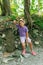 Tired child in panama hat leaning arm on rock take seat on stone in forest with tall trees. Little girl in comfortable