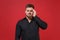 Tired displeased young bearded guy 20s in classic black shirt posing isolated on red wall background studio portrait