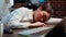 Tired employee sleeping on workspace desk, awaken by coworker, laughing