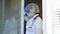 Tired female doctor in protective suit walks to the window, takes off her medical mask, closes her eyes from fatigue