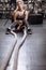 Tired female sportswoman sitting on the floor with battle ropes