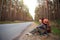 Tired female tourist sits on the side of the road with huge backpack and a mat. Domestic tourism, independent travel alone,