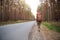 Tired female tourist walking on the roadside with big backpack. Domestic tourism, independent travel alone, hitchhiking, hiking,