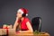 Tired girl elf listen to the music in headphones, sitting at the table with Xmas gifts. Gray background