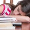 Tired girl sleeping over her laptop with a stack of books on the table