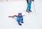 Tired kid in warm blue overalls fell and lies on the snow, resting from skiing lesson