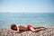Tired little boy in red shorts lying on stone beach near ocean sunbathe during summer holiday travel activity with copy space