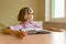 Tired little girl student looks out the window while sitting at her desk with a big book. School, education, knowledge and