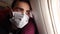 Tired man in a medical face protective mask sits on an airplane and looks out the window