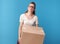 Tired modern woman in white shirt with cardboard box on blue